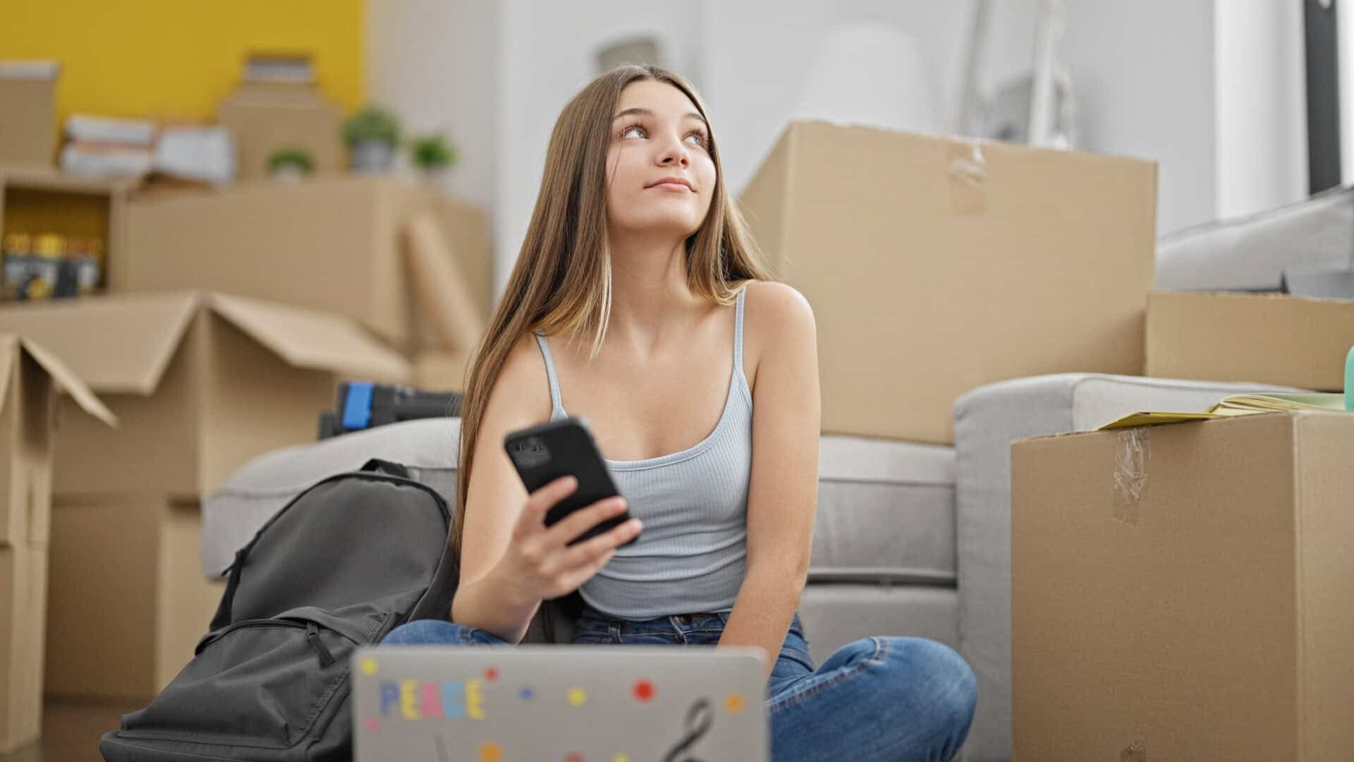 Student sitting among packed moving boxes and personal belongings, preparing to move accommodation.